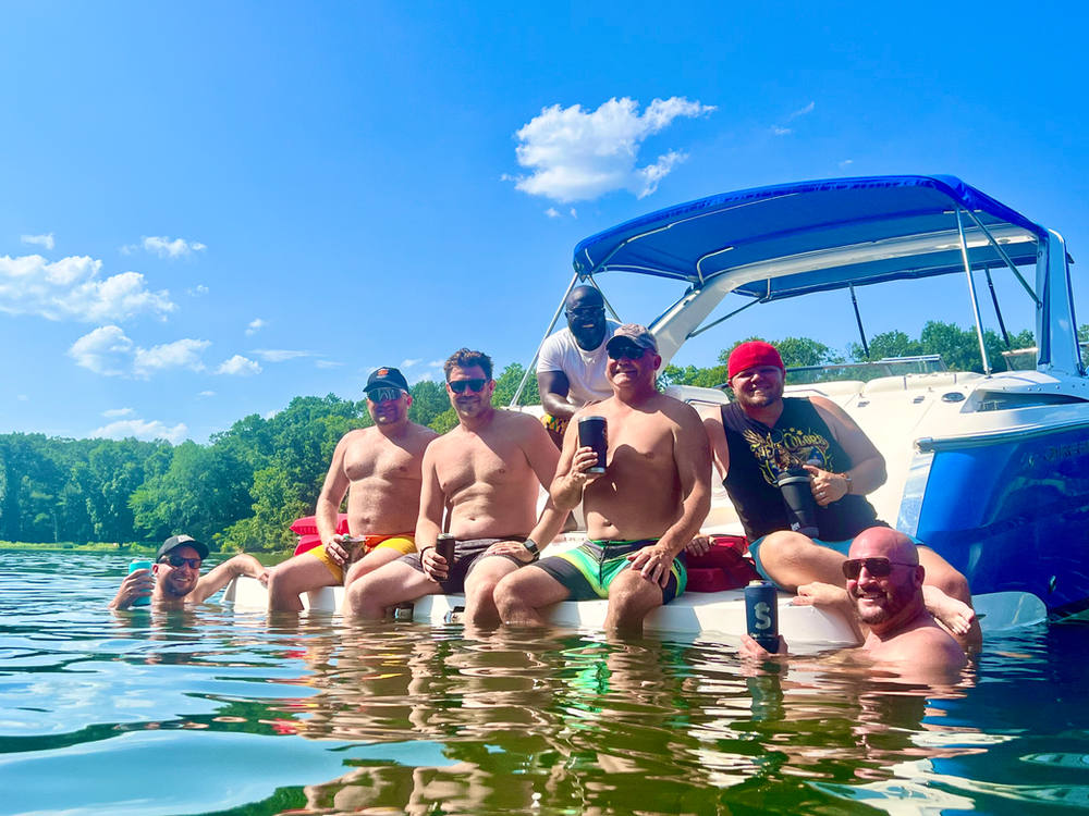 Bachelor party hanging out on the swim platform with drinks, feet in the water